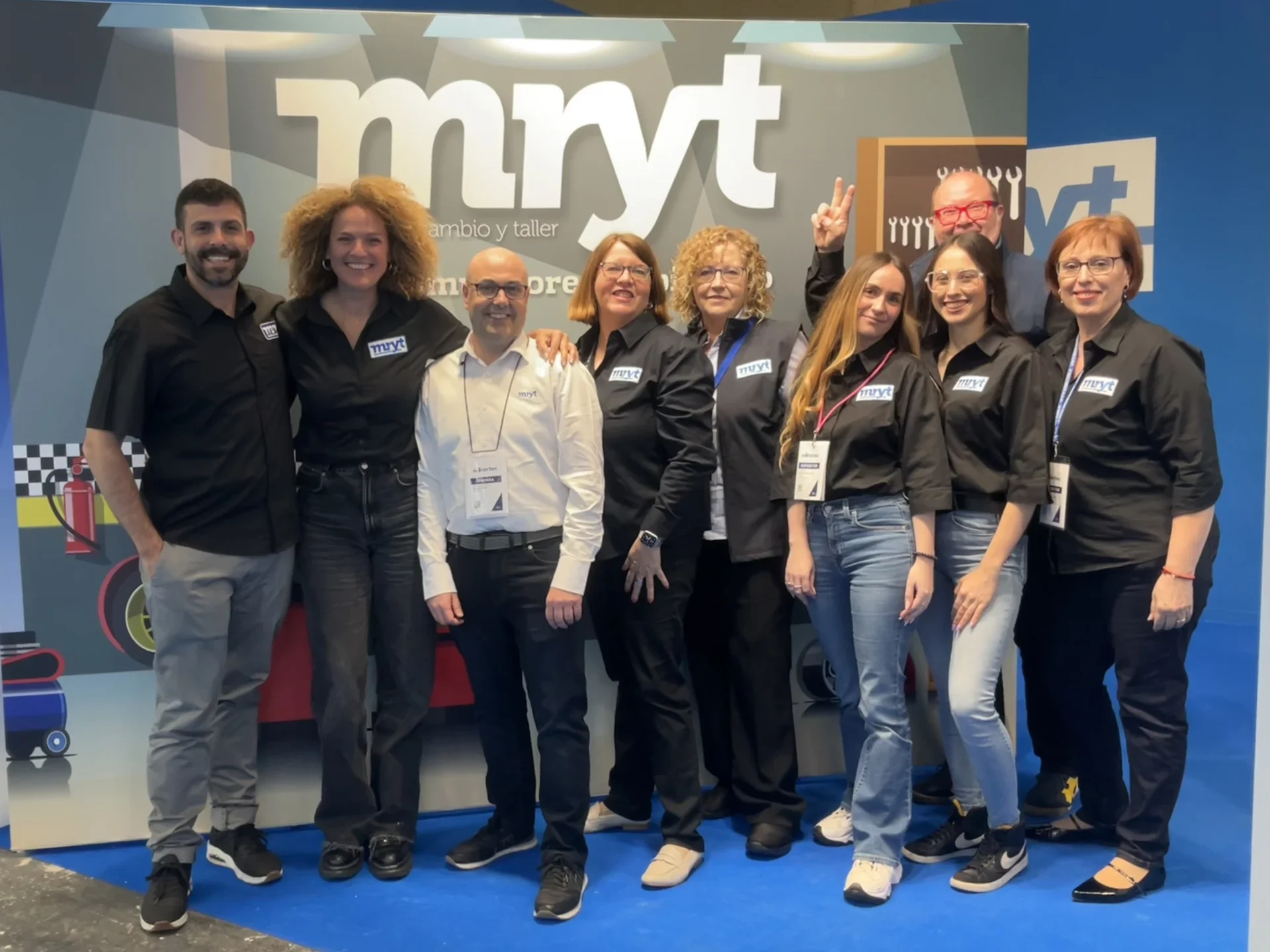 Nueve personas con camisetas negras posan y sonríen frente a un fondo con la marca "mryt" en un evento posventa de Motortec 2025.