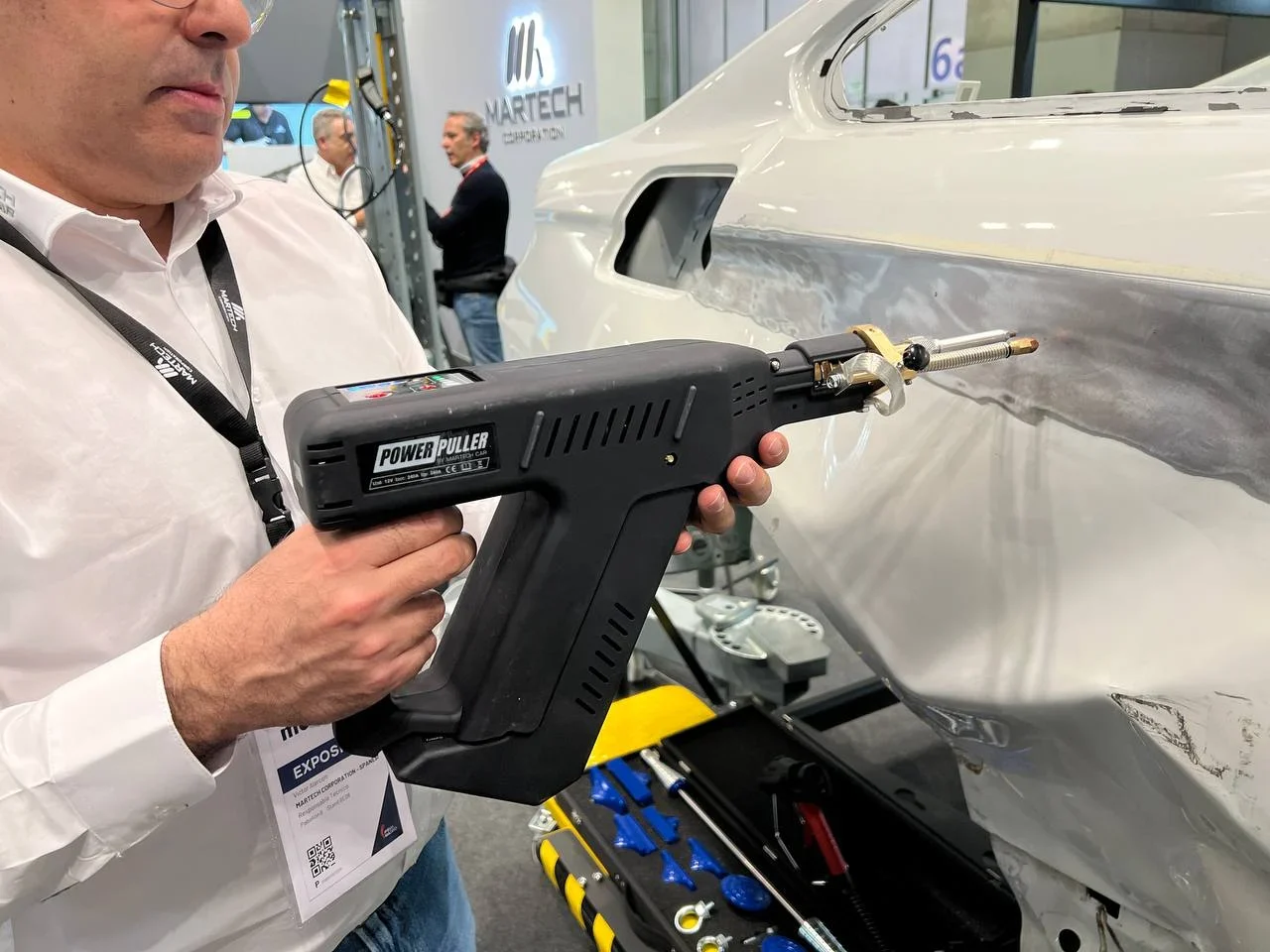 Persona que utiliza una herramienta extractora eléctrica para reparar la carrocería de un automóvil en un taller de reparación de automóviles.
