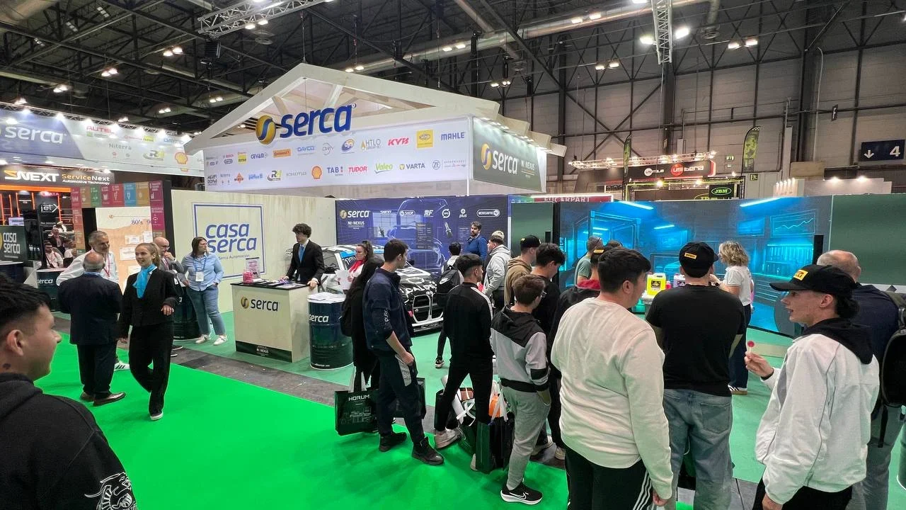 La gente se reúne alrededor del stand de Serca en una feria comercial concurrida, con exhibidores y pancartas visibles.