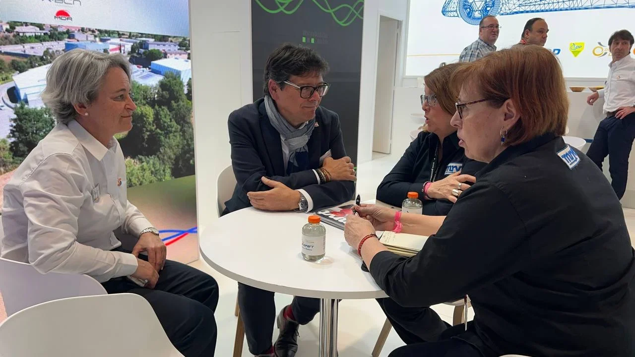 Cuatro personas están sentadas alrededor de una mesa pequeña y conversan en lo que parece ser un evento empresarial o una exposición.