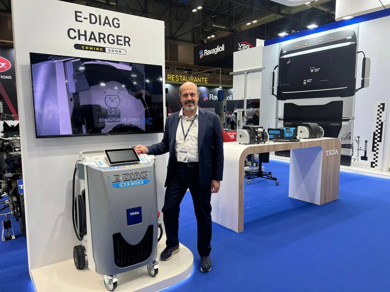 Un hombre se encuentra junto a una máquina de carga E-DIAG en un stand de feria con exhibiciones de repuestos para camiones.