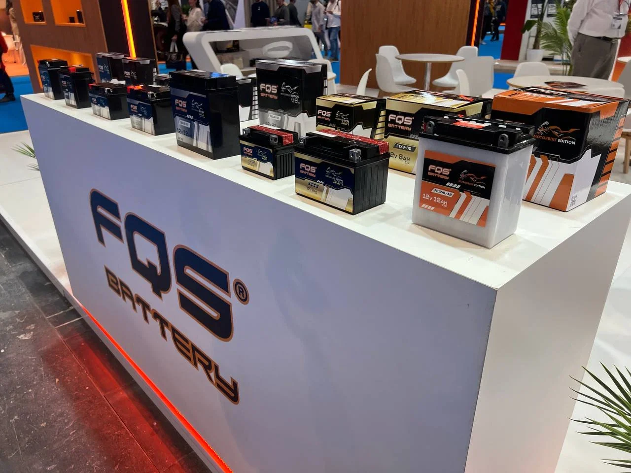 Varios productos de batería FQS se muestran en un stand blanco en una exposición o feria comercial.