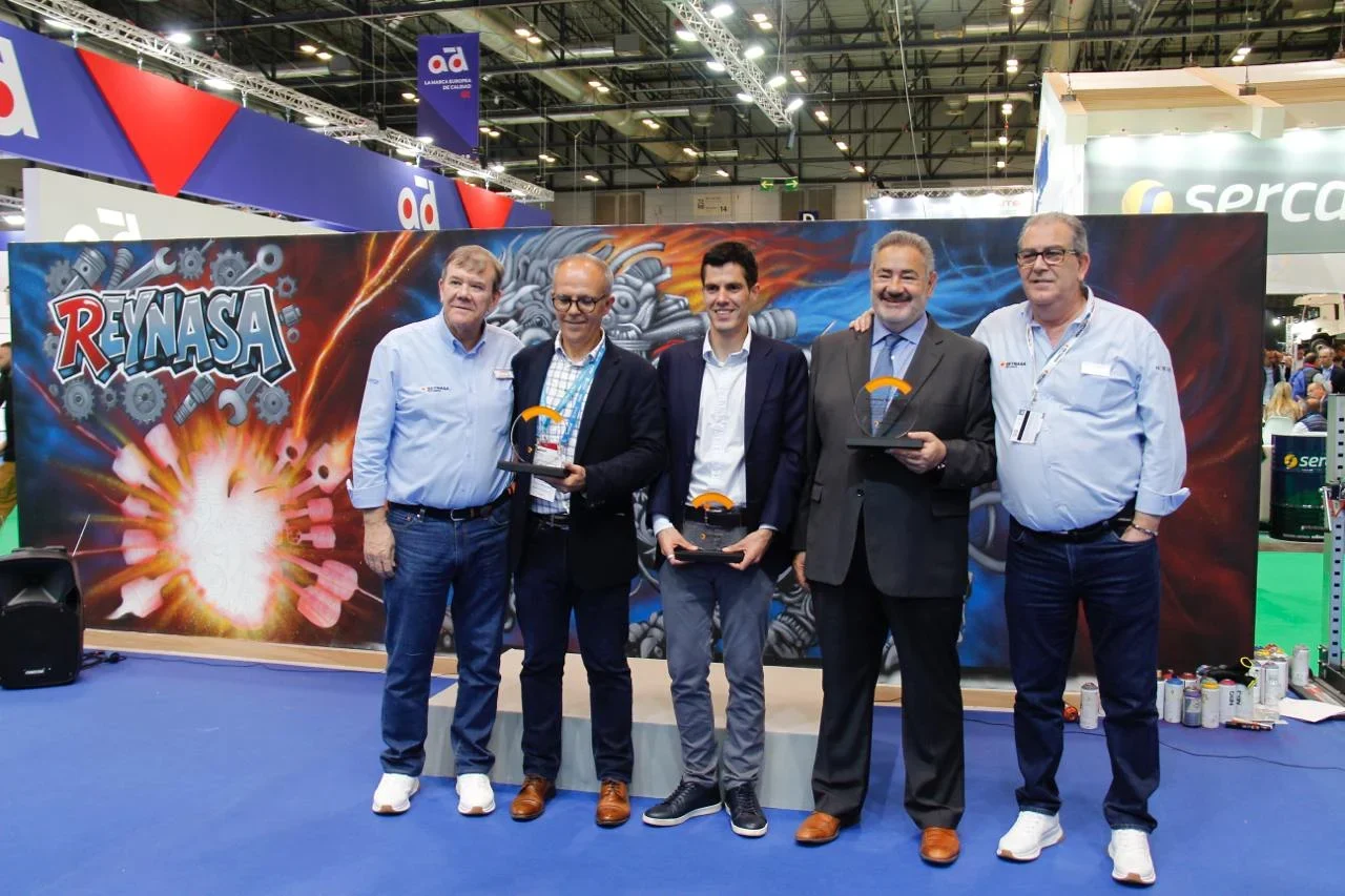 Cinco hombres posan frente a una pancarta de RENASA, tres de ellos sosteniendo trofeos, en una convención o feria comercial.