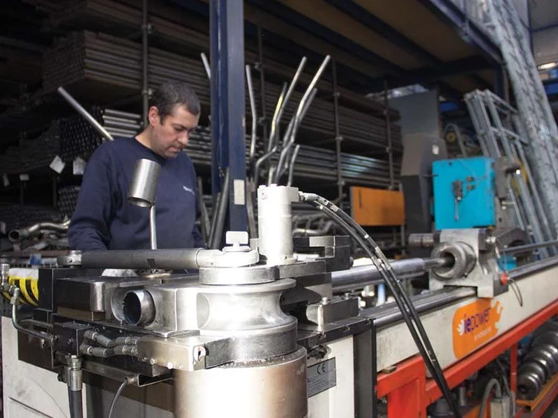 Hombre operando maquinaria profesional en una fábrica con tuberías y equipos metálicos, especializado en fabricación personalizada de sistemas de escape.