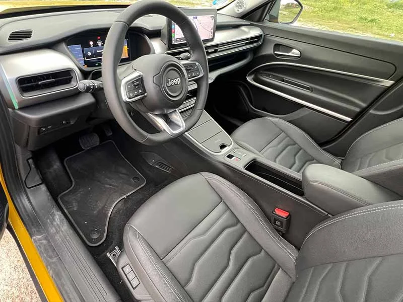 Interior del automóvil Jeep con asientos de cuero negro, pantalla táctil y diseño de tablero moderno.
