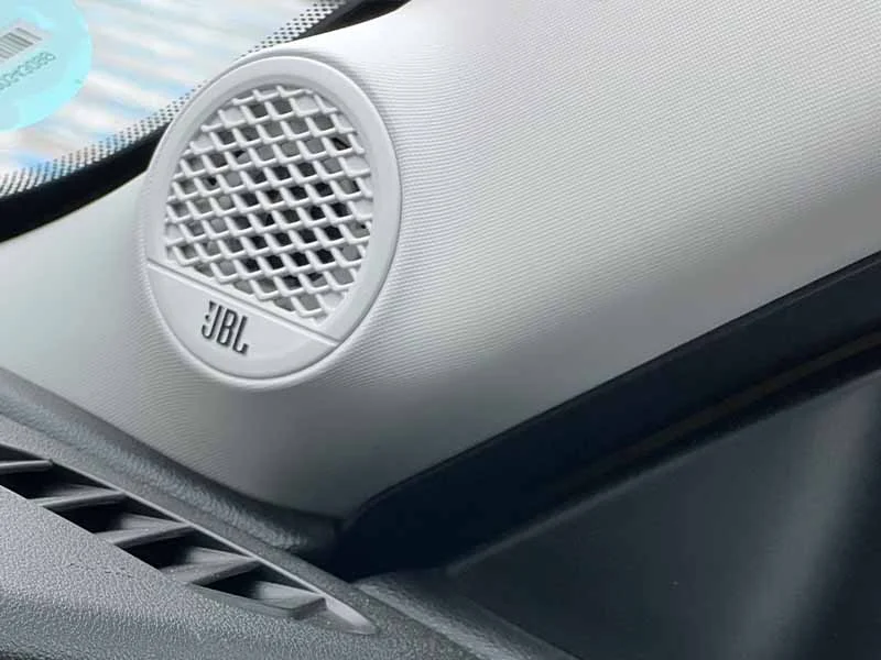 Primer plano de un altavoz de automóvil JBL montado en el tablero de un vehículo cerca del parabrisas.