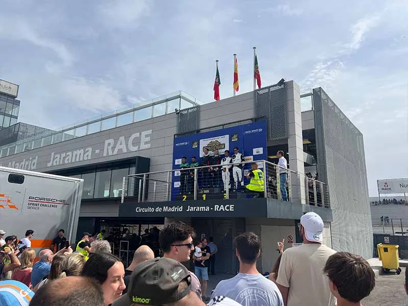 La gente observa cómo los ganadores de las carreras suben al podio en el circuito del Jarama bajo banderas ondeantes, celebrando sus victorias al más puro estilo de una fiesta.
