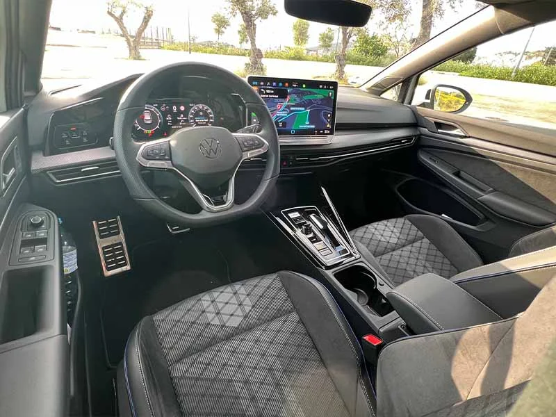 Moderno interior del Golf R-Line con tablero digital, navegación con pantalla táctil y asientos negros acolchados, que luce el innovador motor 1.5 eTSI, estacionado al aire libre: una referencia eterna en diseño automotriz.