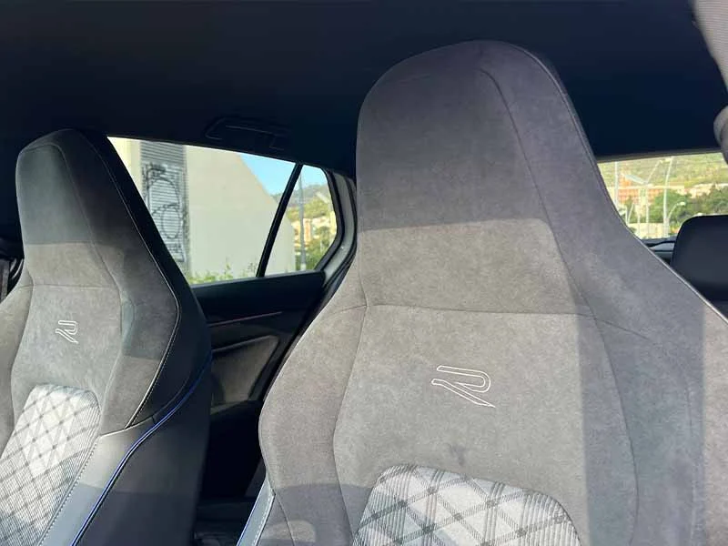 Dos asientos delanteros con tela gris y un logotipo “R”, vistos desde el asiento trasero a la luz del día, que muestran el interior deportivo del Golf R-Line 1.5.