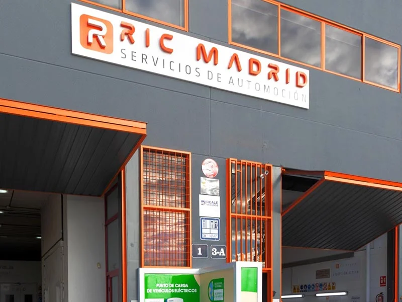 Entrada del centro de servicio de automoción RIC Madrid con señalización naranja y blanca sobre la puerta, reflejando su compromiso con la sostenibilidad.