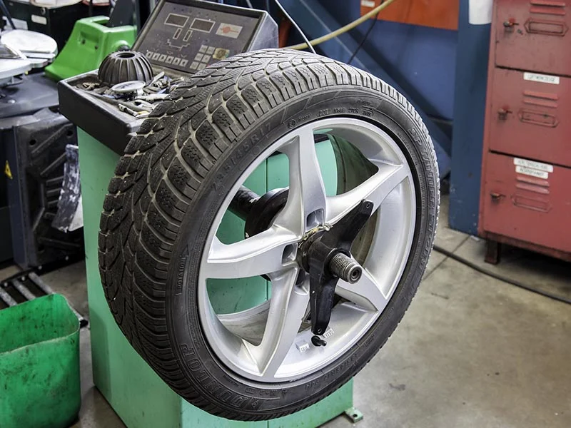 Un neumático de coche montado en una equilibradora de ruedas en un taller mecánico, con piezas de alta calidad de Recomotor desguace en Lleida.