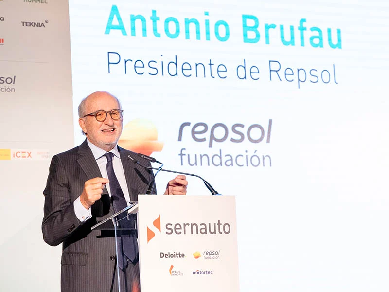 Antonio Brufau habla en un podio durante el Encuentro SERNAUTO, con una pantalla detrás que muestra "Presidente de Repsol", ADN España y logotipos.