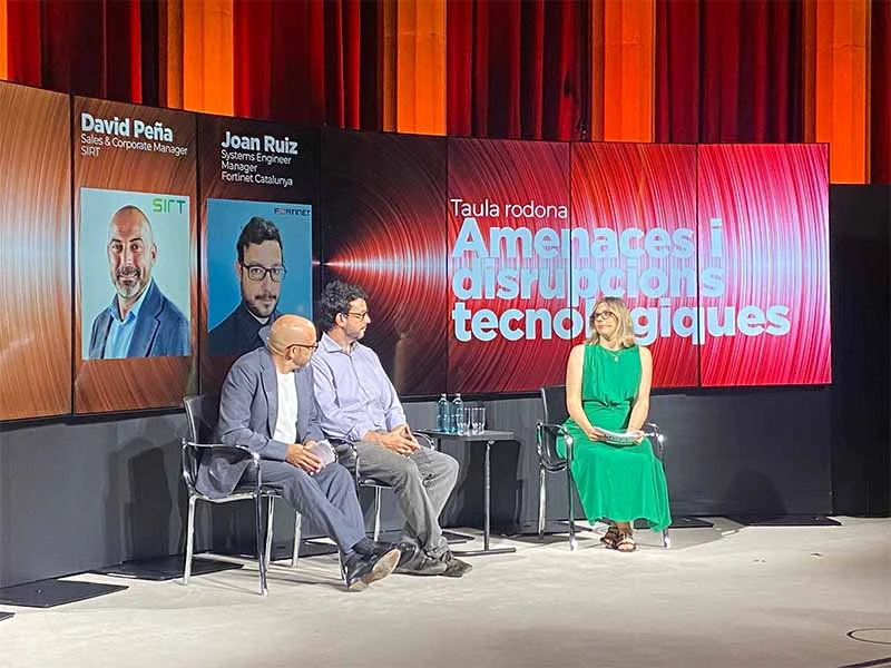 Tres panelistas hablan en el escenario de la Jornada del Metall 2025, con un moderador de la UPM sentado a su lado y una pantalla detrás.