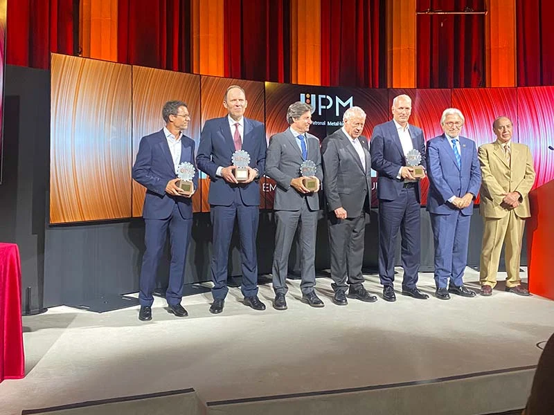 Siete hombres trajeados suben al escenario de la Jornada del Metal 2025, cinco de ellos con premios en la mano, frente a un gran telón de fondo con la marca UPM.