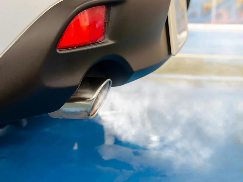 Primer plano del tubo de escape de un automóvil que emite menos humo, estacionado sobre una superficie azul, ayudando a proteger nuestro planeta.