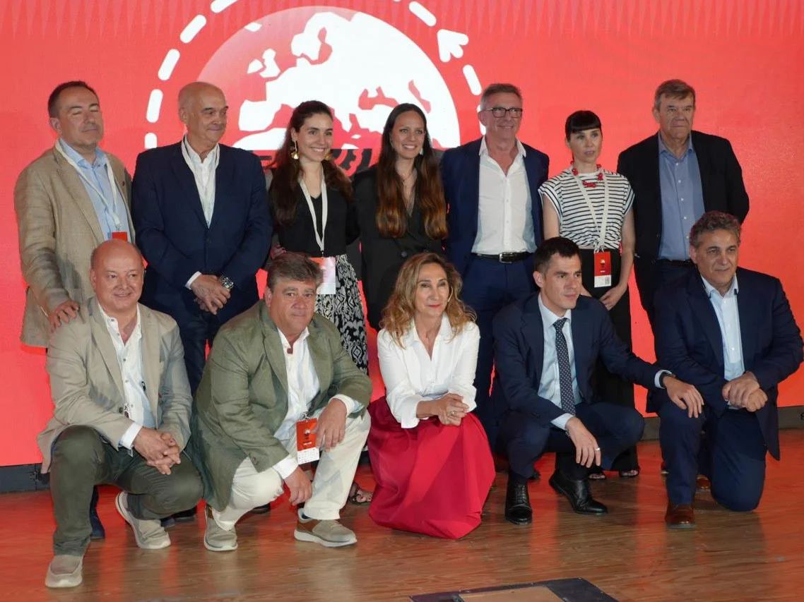 Grupo de personas vestidas de negocios posando juntas frente a un fondo rojo con un diseño de globo blanco.