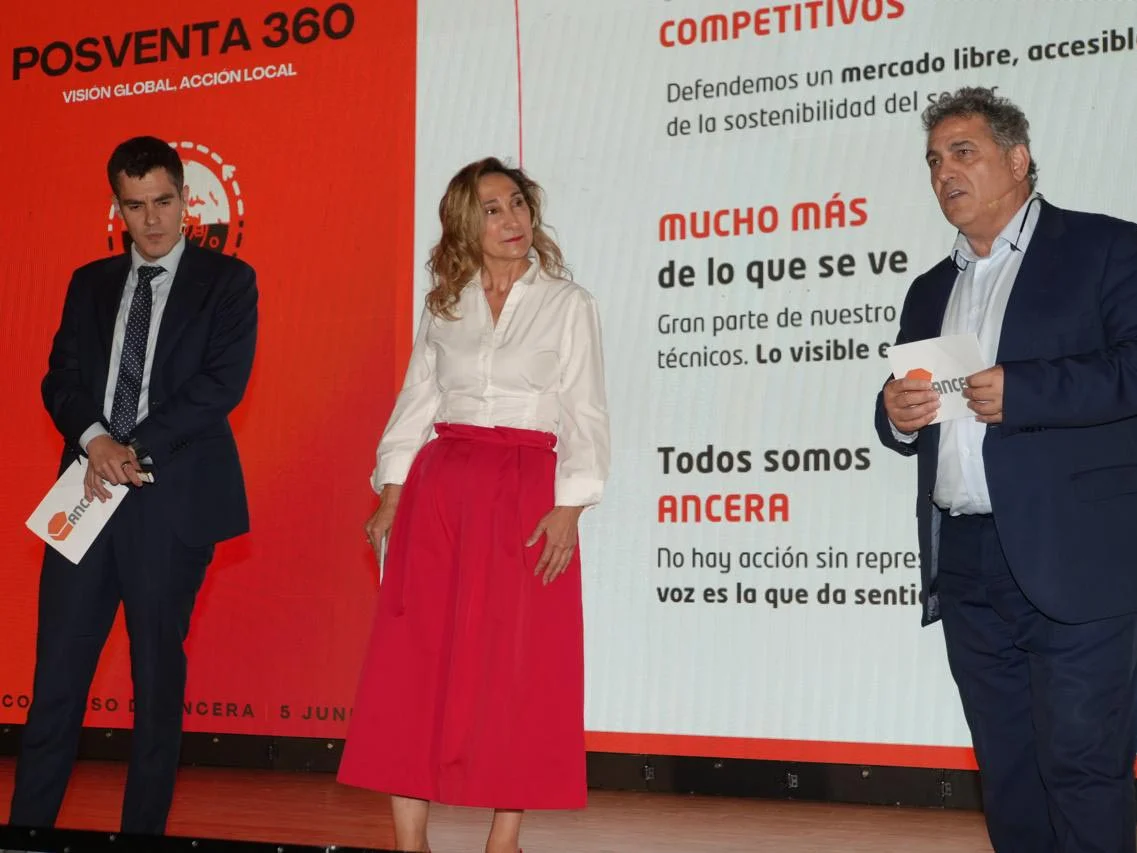Tres personas vestidas de negocios hablan en el escenario frente a una pantalla grande con texto en español.