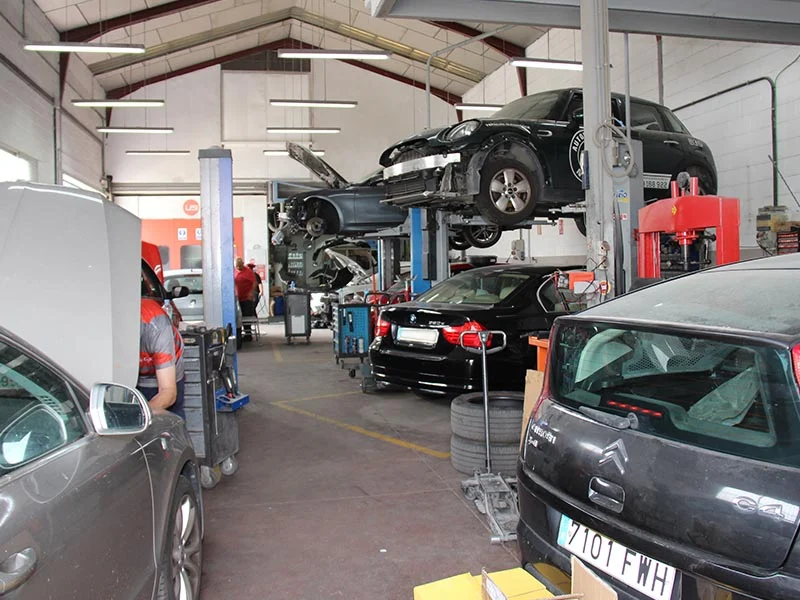 Varios coches siendo reparados en el interior de un concurrido taller de reparación de automóviles, donde los mecánicos trabajan en los vehículos y los clientes y el personal crecen juntos a través de un servicio de calidad.