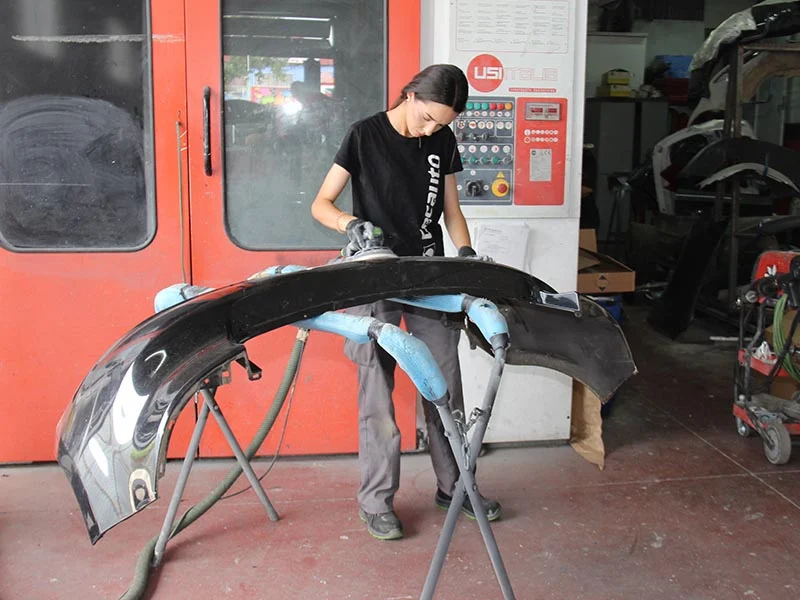 Una persona lijando el parachoques de un coche en un taller de reparación de automóviles, donde el trabajo en equipo y la dedicación ayudan a todos a crecer juntos en el camino hacia la excelencia.