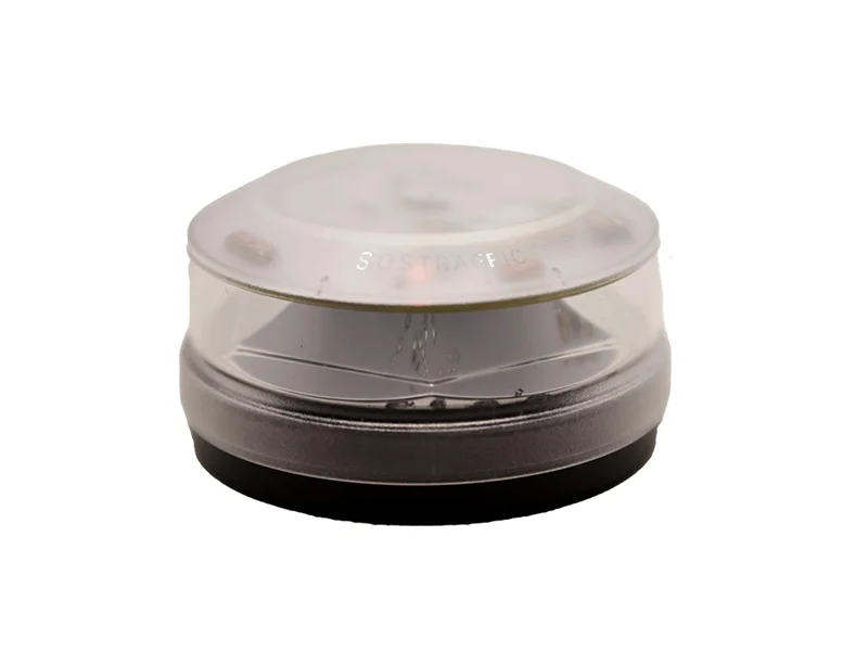 Dispositivo electrónico redondo de plástico transparente y negro con tapa esmerilada, ideal como baliza V-16 para vial de seguridad, representado sobre fondo blanco.