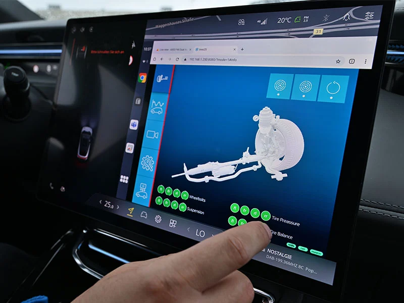 Persona utiliza una pantalla táctil de coche que muestra un modelo en 3D del sistema de neumáticos y suspensión de un vehículo, con el avanzado Sensor de Chasis Inteligente de ZF para la monitorización en tiempo real.