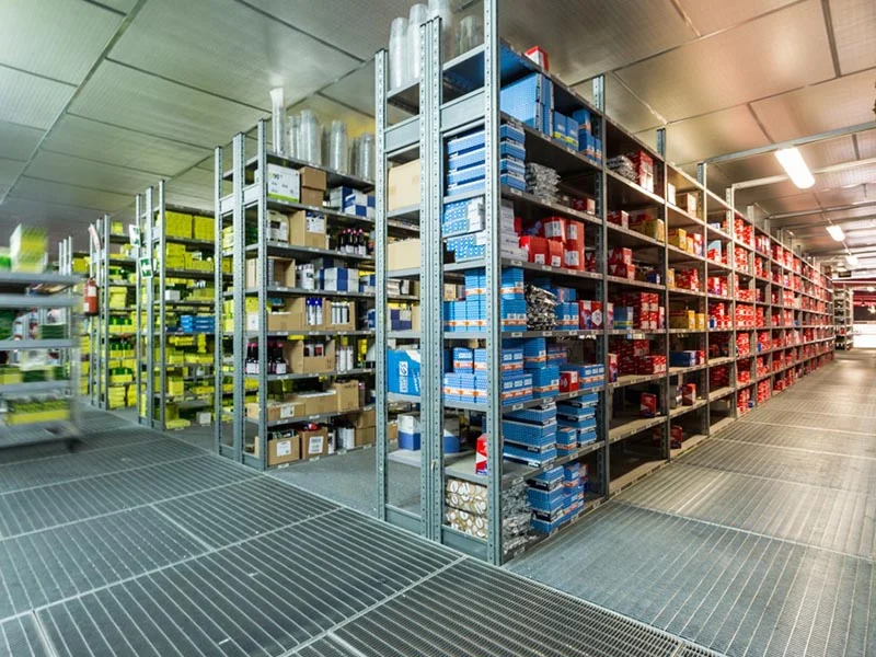 Hileras de estanterías metálicas repletas de cajas y artículos diversos en un almacén bien iluminado, diseñado con éxito y cuidando a las personas que trabajan y almacenan productos aquí.
