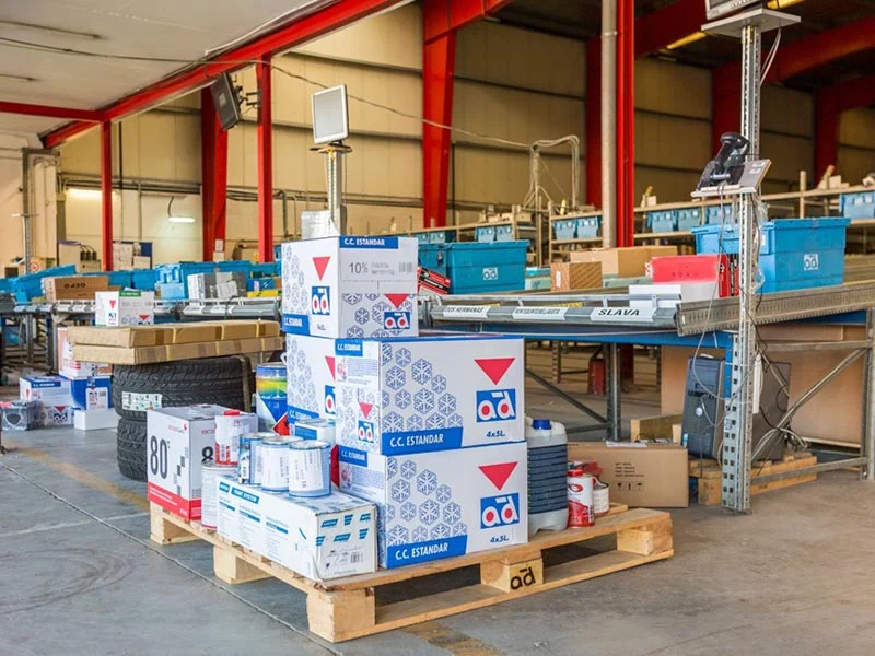 Almacén con cajas y paquetes apilados en un palé cerca de los puestos de trabajo, donde hay personas cuidando cada paso para garantizar el éxito en cada operación.