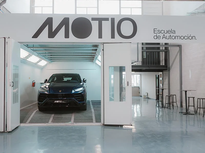 Un coche negro en un moderno garaje de MOTIO Escuela de Automoción, con paredes blancas, puertas de cristal y el innovador sistema de borrador automático.