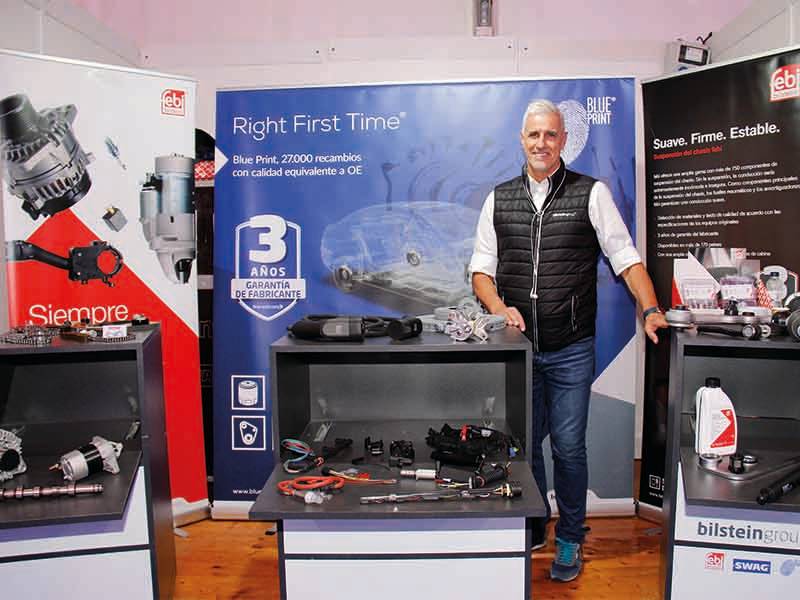 Un hombre se para delante de los expositores de productos de automoción en un stand de una feria, mostrando pancartas y piezas de automóviles, destacando un paso de gigante en tecnología innovadora de vehículos.