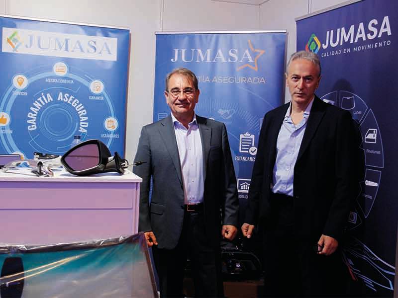 Dos hombres trajeados se paran delante de unas pancartas azules de Jumasa en un stand de un evento, marcando un paso de gigante para la empresa.