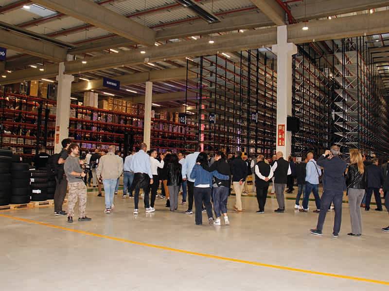 Un grupo de personas de pie y reunidas en el interior de un gran almacén con altas estanterías de almacenamiento, marcando un paso de gigante en sus operaciones.