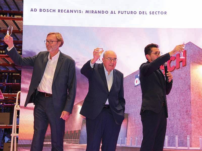 Tres hombres trajeados levantan copas en el escenario ante un cartel de Bosch y una pantalla de presentación en español, celebrando un paso de gigante.