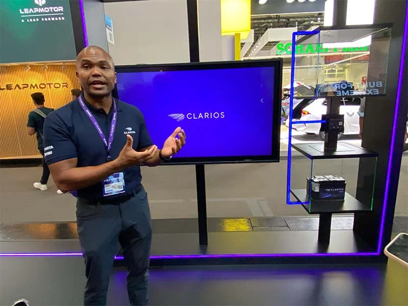 Un hombre frente a una pantalla con el logotipo de Clarios en un stand de la feria IAA Mobility tech, en el que se destacan innovaciones como la batería de competición Optima.
