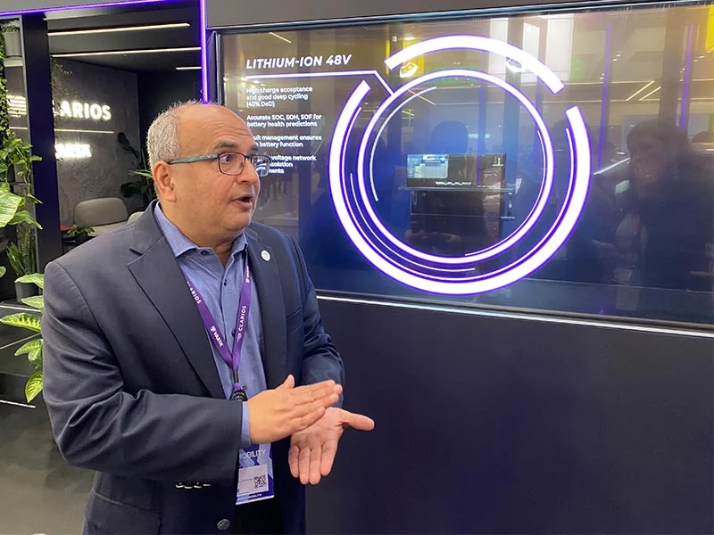 Un hombre de traje gesticula mientras habla delante de un expositor sobre la tecnología de iones de litio de 48V y la batería de competición Optima en el stand de CLARIOS durante la IAA Mobility.