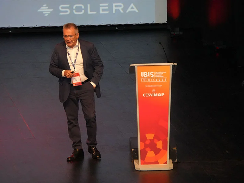 Un hombre trajeado habla en el escenario de un acto de IBIS Iberia 2022, de pie junto a un podio.