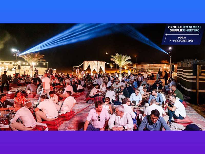 Un nutrido grupo de personas sentadas sobre alfombras en un evento nocturno al aire libre con luces y palmeras en Dubai durante la Reunión Mundial de Proveedores GROUPAUTO 2025.