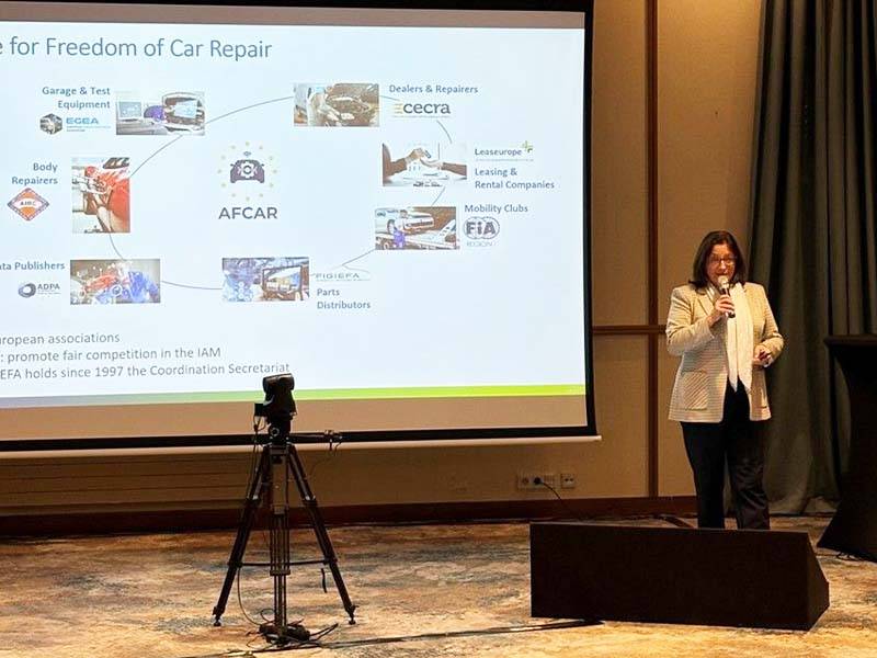 Una mujer habla en el escenario junto a una pantalla que muestra una presentación de "Freedom of Car Repair" en el evento Global One Automotive.