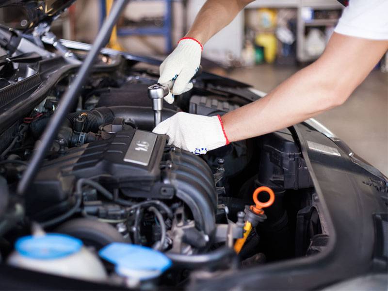 Mecánico con guantes utilizando una carraca para trabajar en el motor de un coche en un garaje, proporcionando soporte técnico para preparar el vehículo para el invierno.