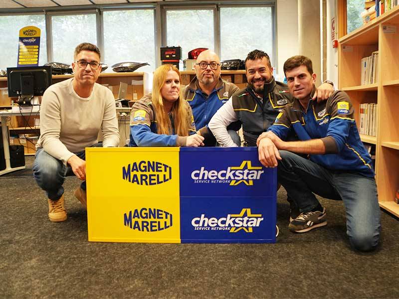 Cinco personas posan en el interior detrás de los carteles de Magneti Marelli y Checkstar, representando al equipo multinacional de Parts & Services, todos sonriendo a la cámara.