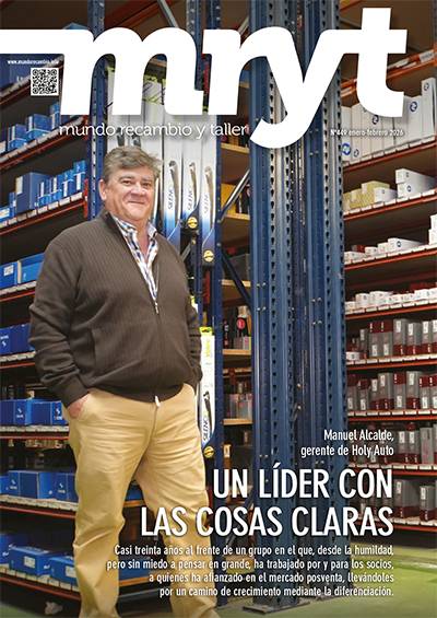 Hombre de pie en un almacén de piezas de automóvil, sonriendo con los brazos cruzados; al fondo se ven estanterías con cajas, piezas y un borrador automático.