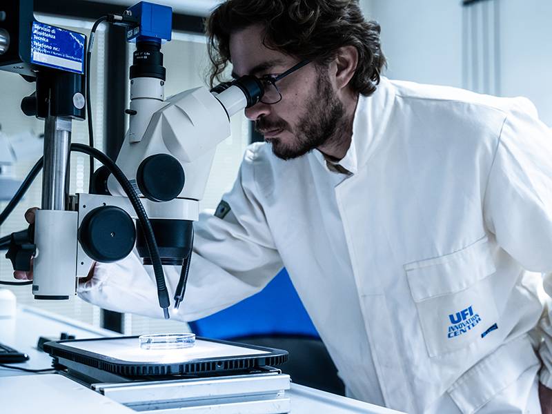 Científico con bata examinando una muestra al microscopio en un laboratorio.