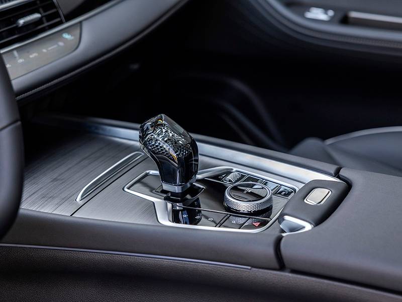 Detalle de la palanca de cambios de cristal del Ebro S700 y del panel de control central con botones y diales, que ejemplifican el lujo del PHEV en esta nueva era de conducción sofisticada.