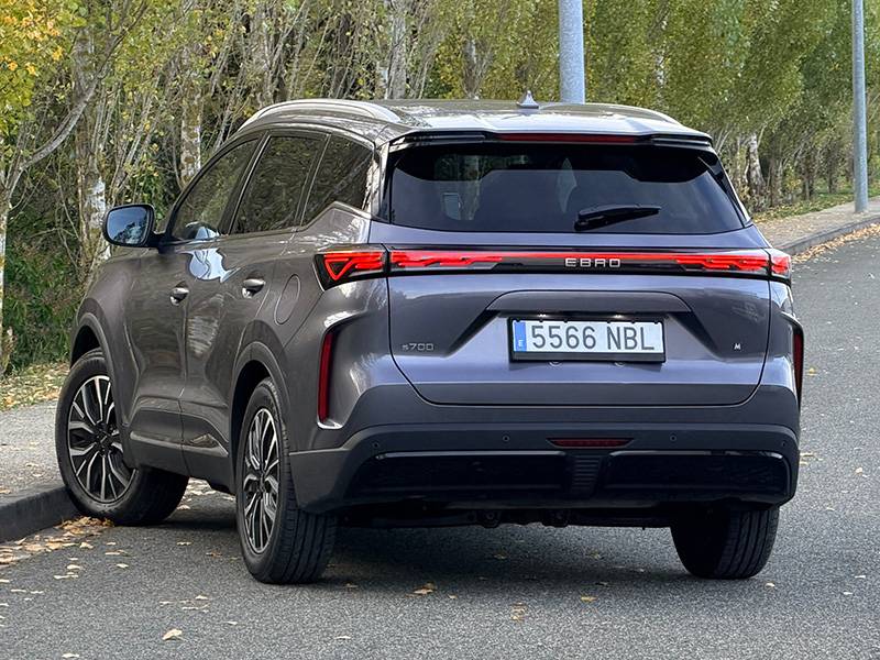Lujoso SUV Ebro S700 PHEV aparcado en una calle cerca de árboles, visto desde atrás con una matrícula española visible.