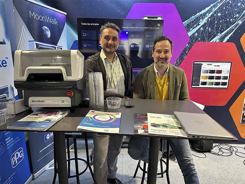 Dos hombres en un stand con folletos, ordenadores portátiles y equipos en una feria tecnológica o comercial, hablando del Balance de Equipia 2026 y del éxito de asistencia al evento.