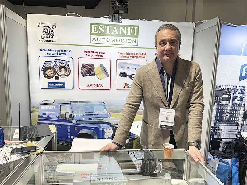 Hombre de pie en un stand de piezas de automoción con la pancarta de Estanfi Automoción y el expositor de Land Rover detrás, destacando la asistencia clave para el éxito de oferta y el Balance de Equipia 2026.