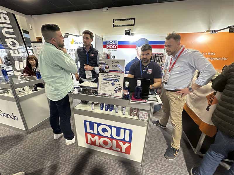 Cuatro hombres conversan de pie en un stand de Liqui Moly en un evento de interior, discutiendo la oferta y el Balance de Equipia 2026, con varios productos expuestos en el mostrador.