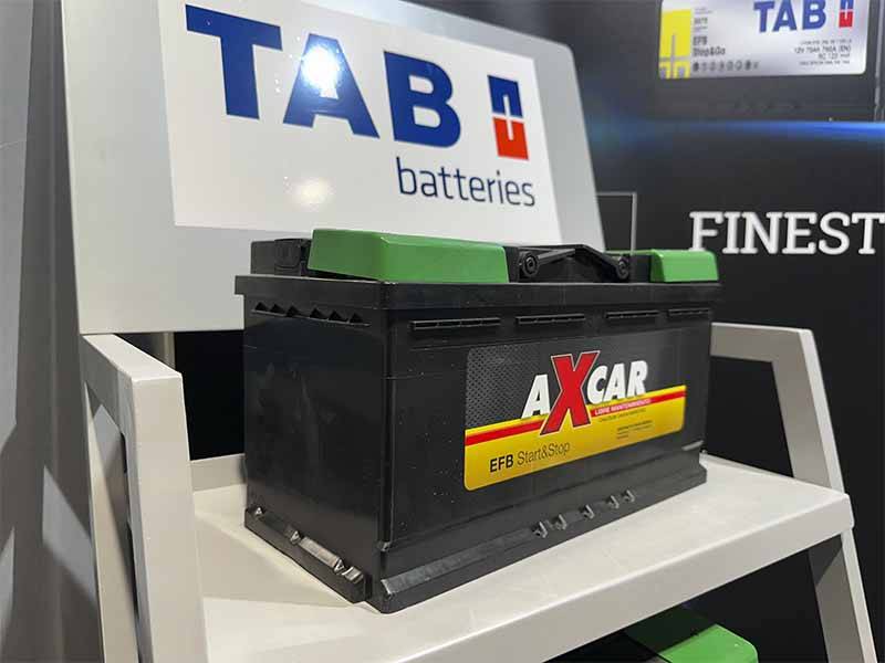 Una batería de coche AXCAR negra con los extremos verdes, expuesta en una estantería blanca cerca de un cartel de TAB batteries, destaca el éxito de oferta en el Balance de Equipia 2026.