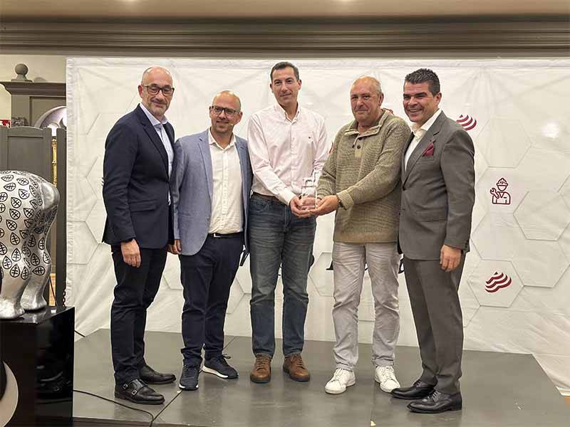 Cinco hombres permanecen juntos en el interior, uno de ellos con un trofeo en la mano, posando ante un fondo blanco con logotipos que celebran el éxito de asistencia y Balance de Equipia 2026.