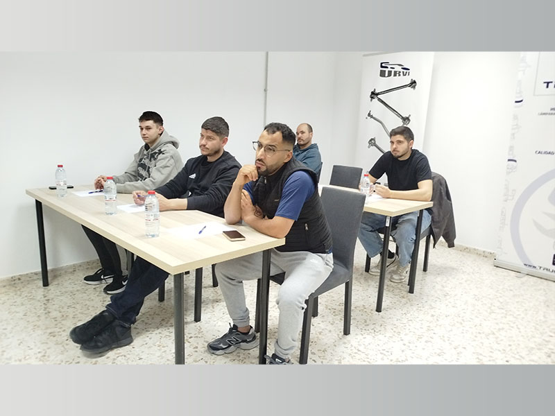 Cinco hombres se sientan en los pupitres de un aula de la Academia URVI, escuchando atentamente, con cuadernos y botellas de agua delante.