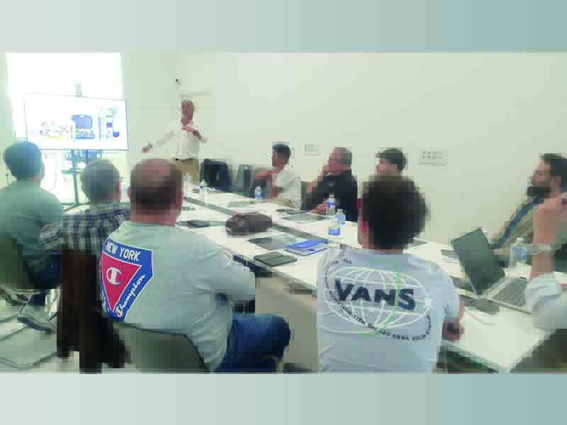 Un grupo de personas en una mesa de conferencias escucha a un presentador de URVI Academy junto a una pantalla en una sala luminosa.
